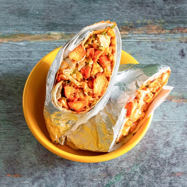 Two foil-wrapped burritos filled with chicken and vegetables, served in a yellow bowl.