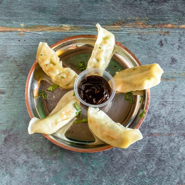 Steamed dumplings arranged in a circle on a metal plate with a small cup of dark sauce.