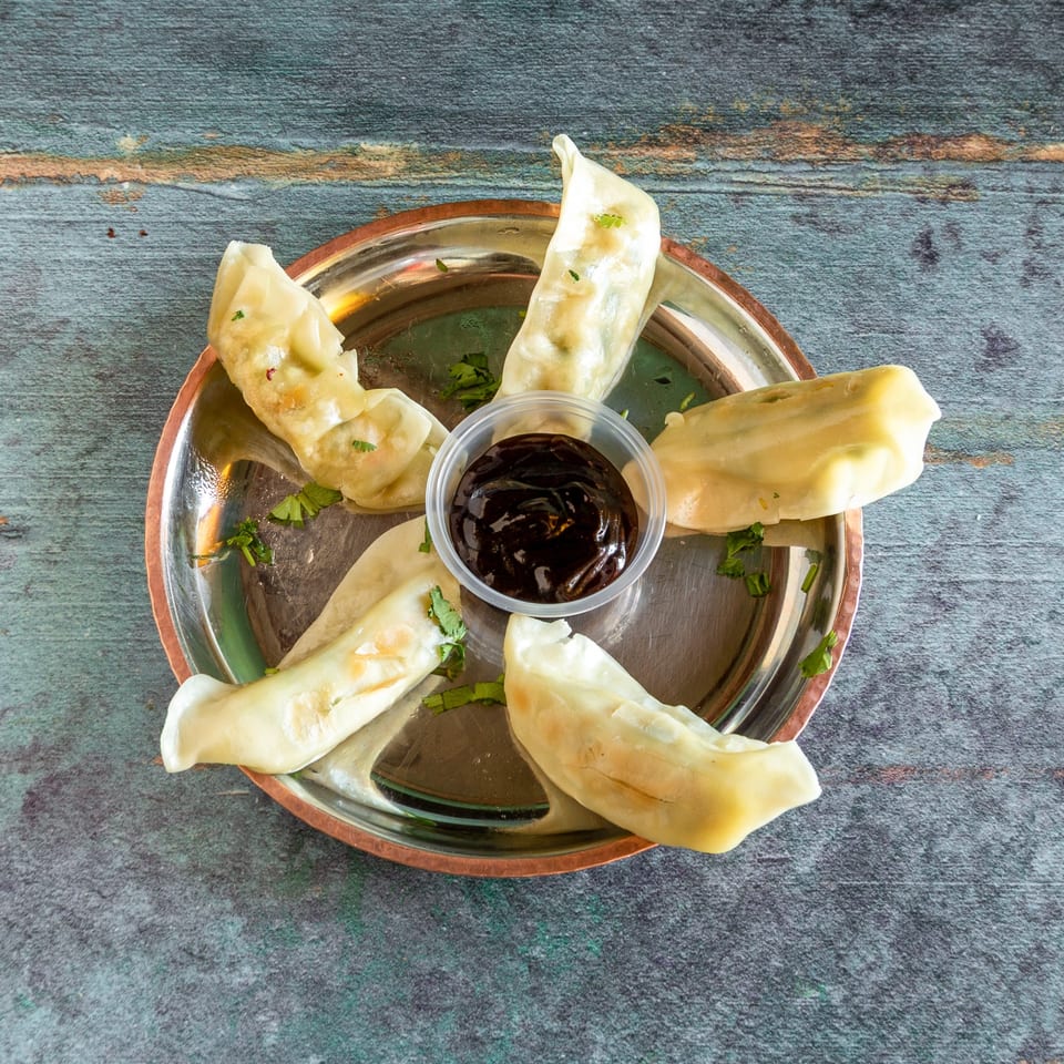 Steamed dumplings arranged in a circle on a metal plate with a small cup of dark sauce.