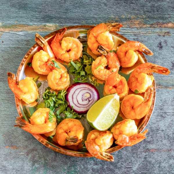 Golden brown shrimp arranged on a copper platter with cilantro, red onion, and lime.