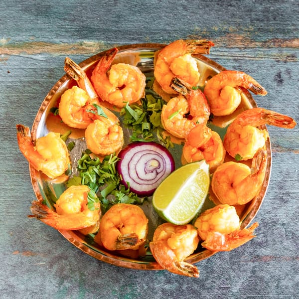 Golden-brown shrimp arranged on a copper platter with cilantro, red onion, and lime.