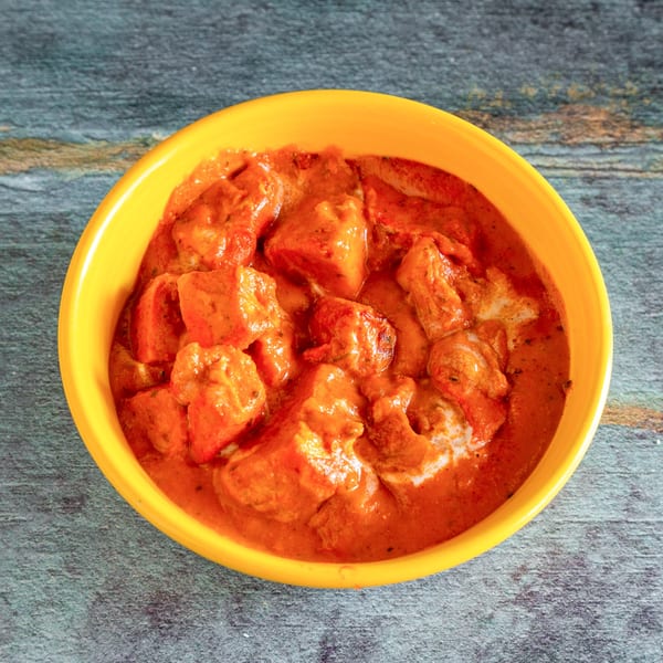 Bright orange paneer tikka masala in a yellow bowl on a rustic grey and brown surface.