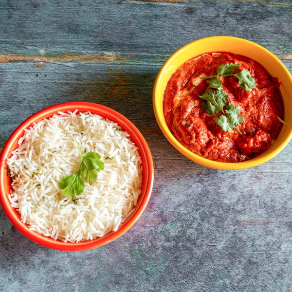A vibrant orange bowl of white rice and a yellow bowl of red curry with cilantro on a rustic table.