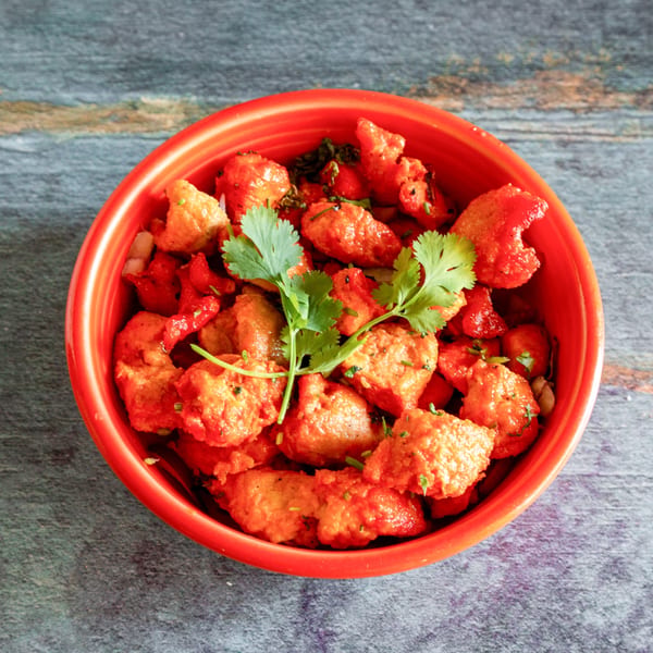 Overhead view of a red bowl filled with vibrant orange chicken pieces, garnished with fresh cilantro.