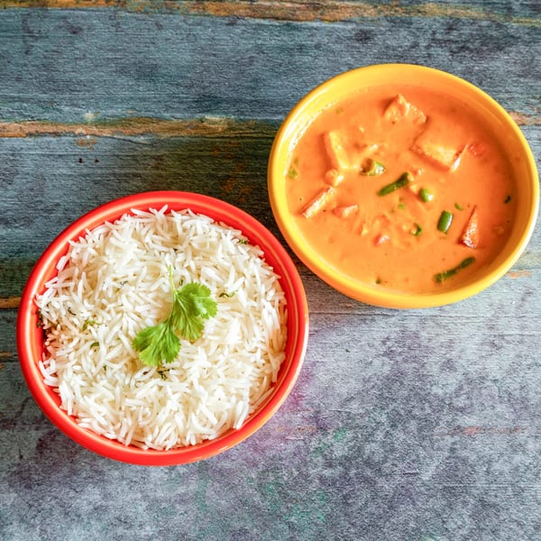 Two bowls of Indian food, one with white rice and cilantro, the other with orange curry.