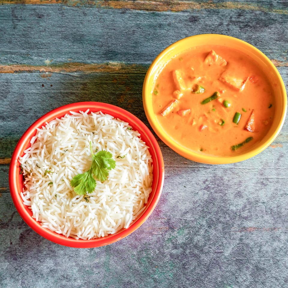 Two bowls of Indian food, one with white rice and cilantro, the other with orange curry.