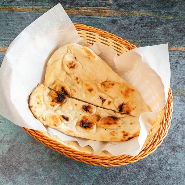 Two pieces of warm naan bread with charred spots, served in a wicker basket lined with parchment paper.