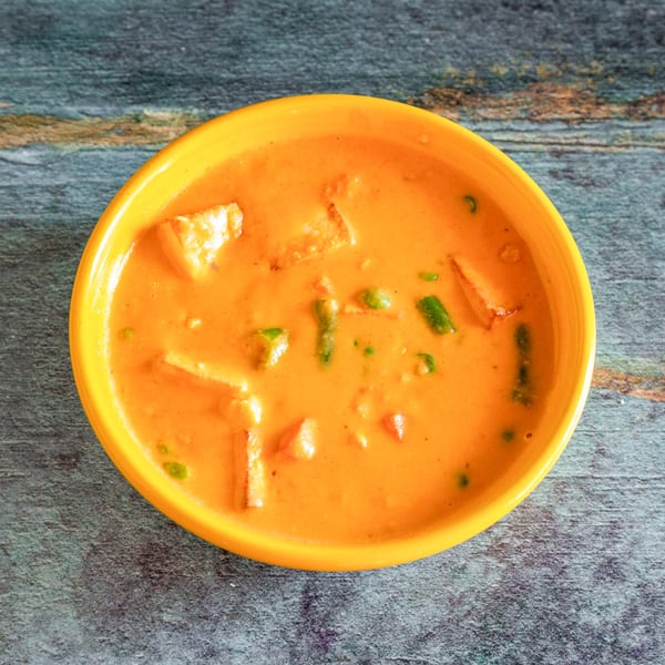 Overhead view of a bright orange bowl filled with paneer butter masala on a grey wooden surface.